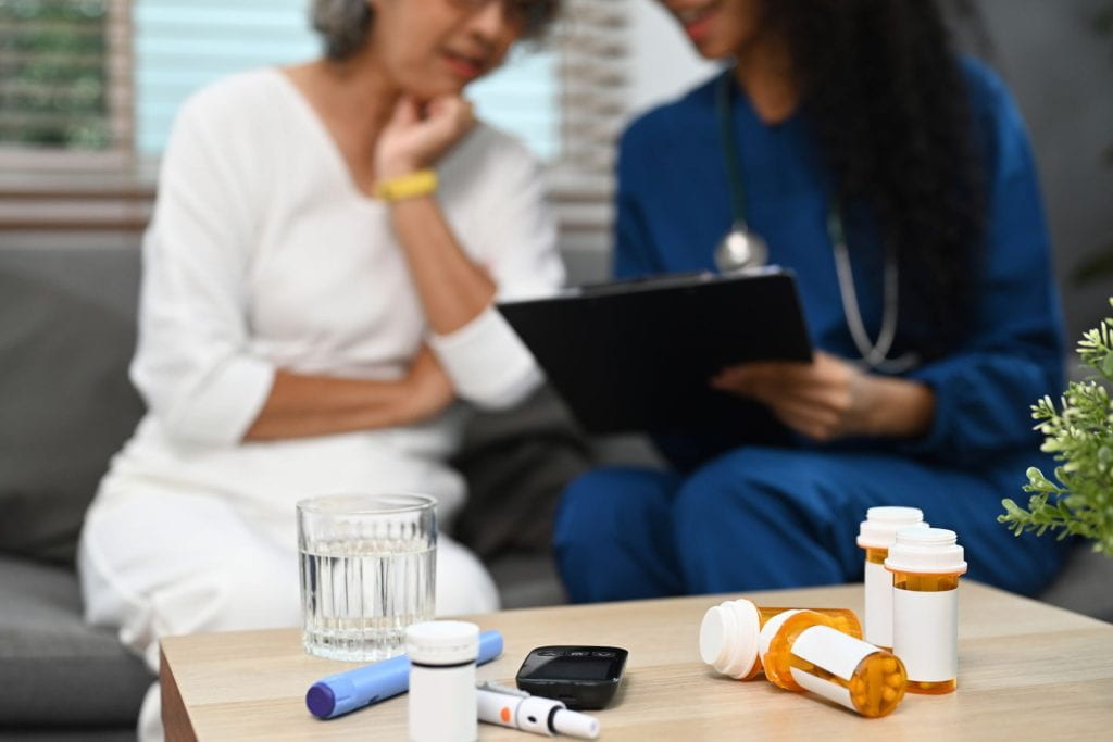 Female doctor and patient looking at laptop together by a table with different medications.